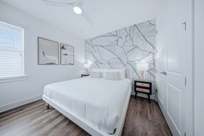 Een slaapkamer met een groot bed, twee nachtkastjes, een plafondventilator en een muur met een bladmotief.