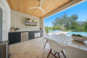 Een keuken met een betegelde spatwand, een plafondventilator en uitzicht op een zwembad en groen.