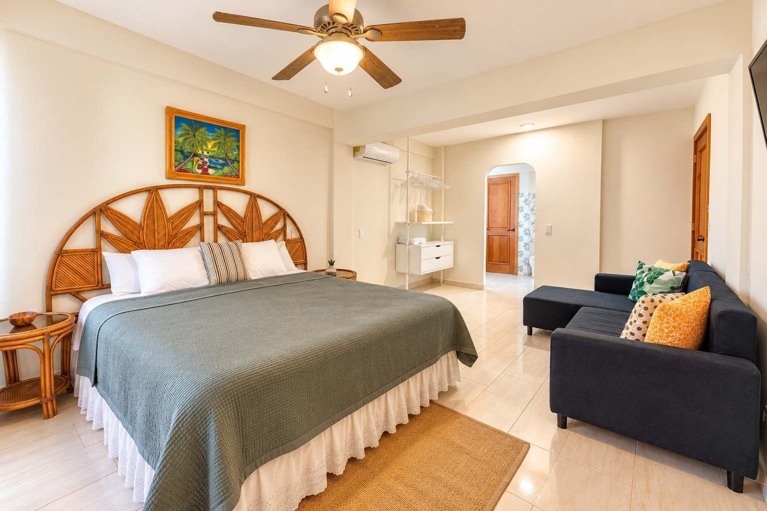 Ein Schlafzimmer mit einem Bett, Deckenventilator, einem Gemälde, einem Nachttisch, einer Kommode, einem Sofa und einem Teppich.