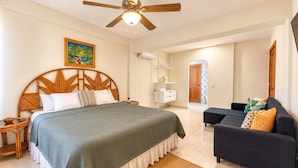 Un dormitorio con cama, ventilador de techo, un cuadro, mesita de noche, cómoda, sofá y alfombra.