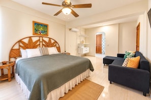 Ein Schlafzimmer mit einem Bett, Deckenventilator, einem Gemälde, einem Nachttisch, einer Kommode, einem Sofa und einem Teppich.