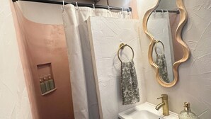 Ein Badezimmer mit Duschvorhang, Waschbecken mit Goldarmatur, Spiegel mit Holzrahmen und Handtuch an der Wand.