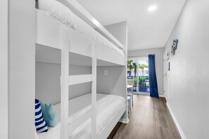 A room with bunk beds, a hallway leading to a balcony, and a view of palm trees. - Gulf Island 612 (Navarre)