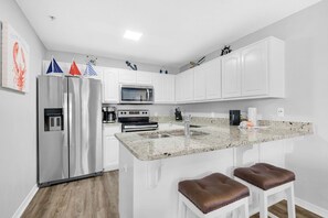 A modern kitchen with white cabinets, stainless steel appliances, a granite countertop, and two stools. - Gulf Island 612 (Navarre)