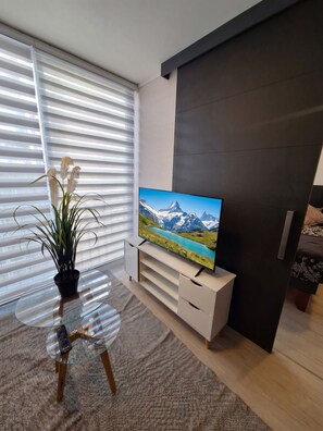 A modern living room with a flat-screen TV on a white entertainment unit, a potted plant, and a glass coffee table. - Borde Vivo Santiago by Domus Travels (Santiago)