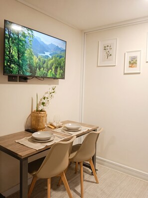 A dining area with a TV mounted on the wall, a table set for two, and framed botanical prints on the wall. - Borde Vivo Santiago by Domus Travels (Santiago)