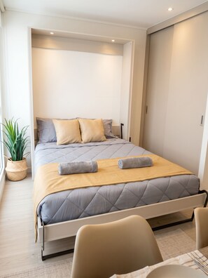 A modern bedroom with a bed, pillows, a bedside table, a plant, and a chair. - Borde Vivo Santiago by Domus Travels (Santiago)
