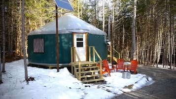 A yurt with a door, a small window, and a solar panel on top. There are orange chairs outside and a wooden ramp leading to the door.