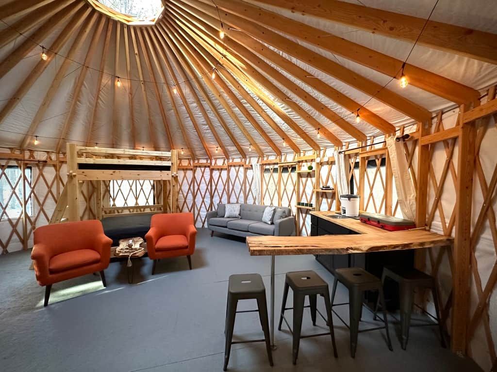 A yurt interior with a sofa, two armchairs, a coffee table, a bar area, and stools.