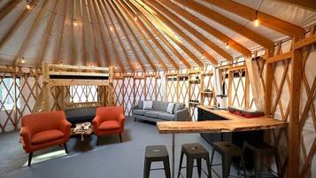 A yurt interior with a sofa, two armchairs, a coffee table, a bar area, and stools.