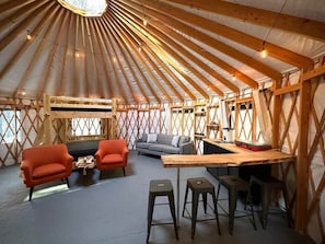 A yurt interior with a sofa, two armchairs, a coffee table, a bar area, and stools.