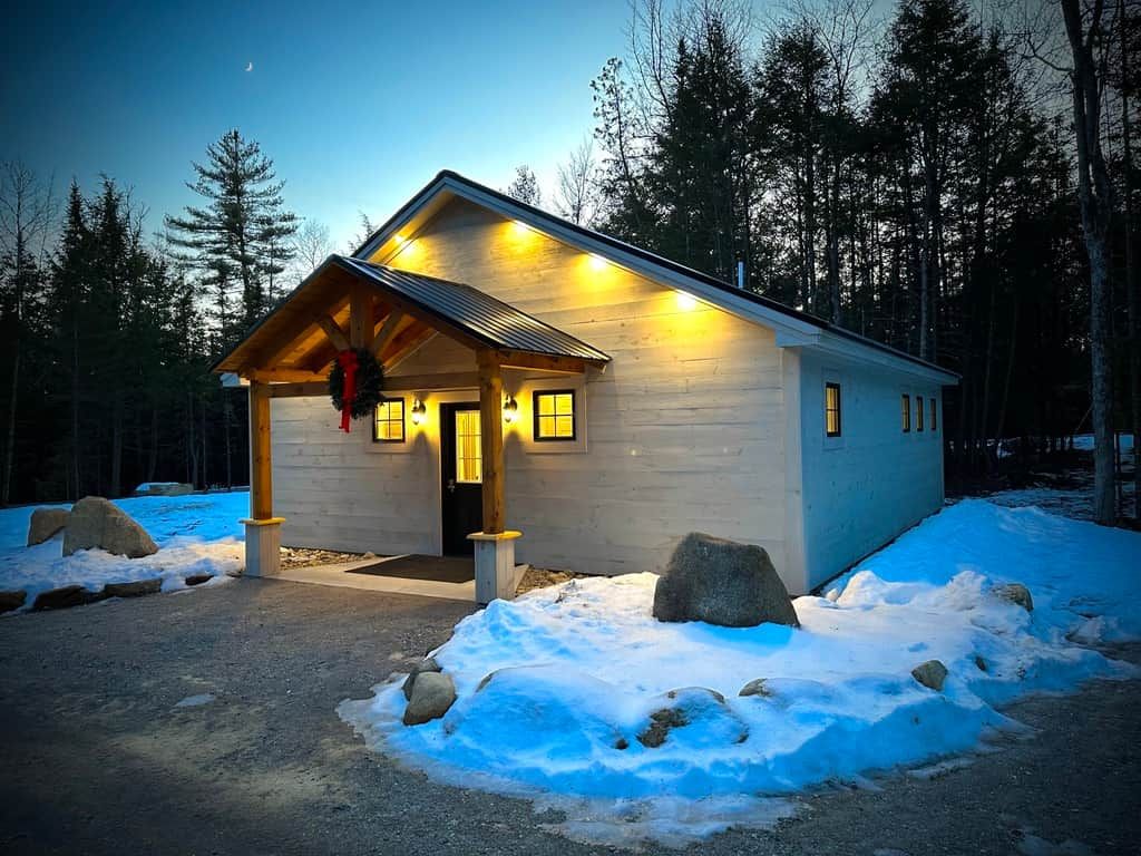 A cabin with a porch, wooden exterior, and a lit entrance.