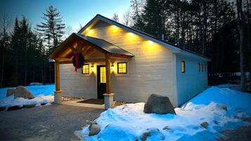 A cabin with a porch, wooden exterior, and a lit entrance.