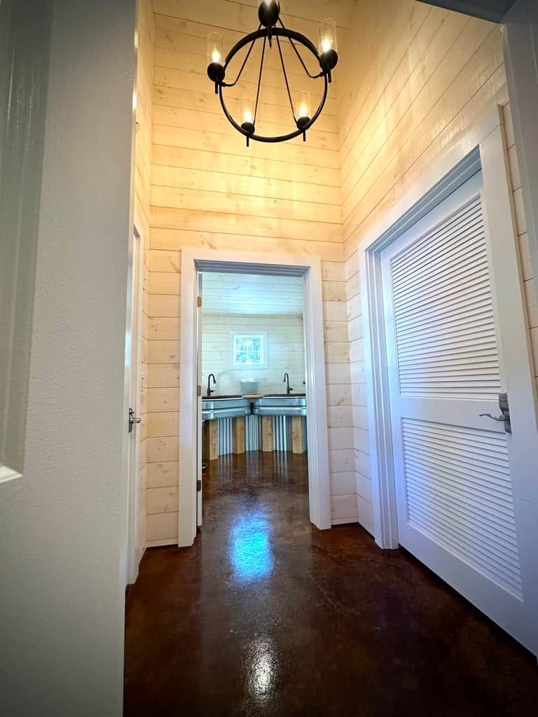 A hallway with wooden walls and a polished floor leading to a bathroom with a sink and mirror.