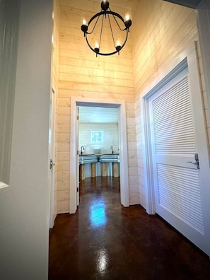 A hallway with wooden walls and a polished floor leading to a bathroom with a sink and mirror.