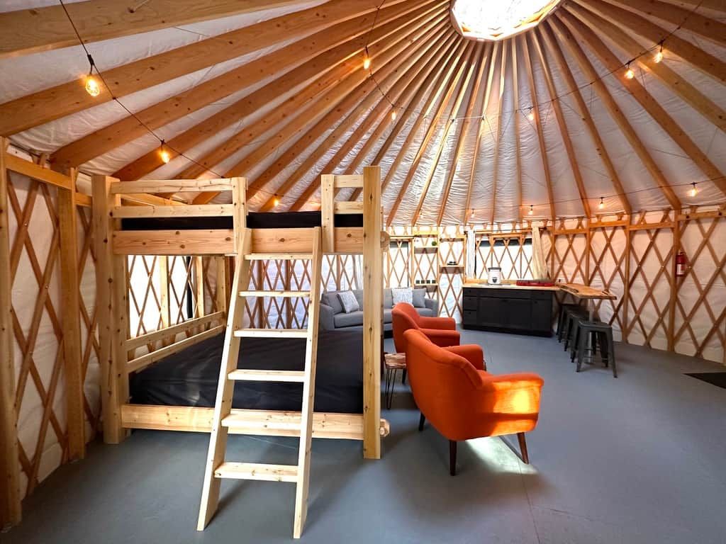 A yurt interior with a wooden ladder, a sofa, and orange chairs.
