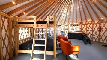 A yurt interior with a wooden ladder, a sofa, and orange chairs.