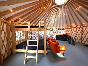 A yurt interior with a wooden ladder, a sofa, and orange chairs.