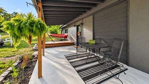 Alpendre coberto com mesa e cadeiras, planta pendente e um guarda-sol vermelho.