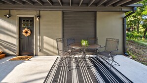 Uma área de varanda coberta com mesa e cadeiras de metal, uma porta decorada com uma grinalda e um tapete de boas-vindas.