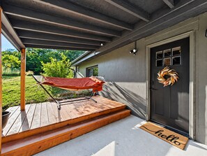 A wooden deck with a hammock, a door with a wreath, and a 'hello' mat.