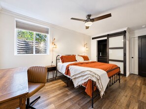 A bedroom with a bed, a desk, a chair, a ceiling fan, and a window with blinds.