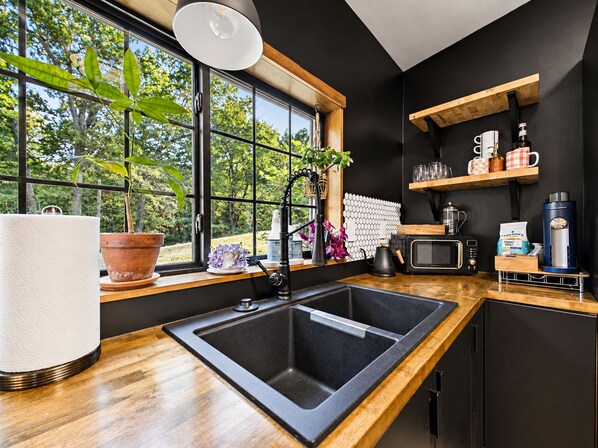 A modern kitchen with a large window, a sink, a microwave, and a coffee machine.