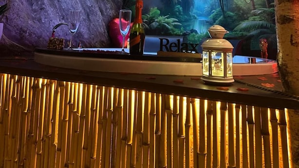 En bar med et tropisk muralmaleri, en vinflaske, et glas og en lanterne.