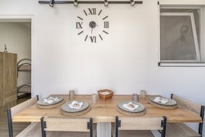A dining area with a wooden table set for four, a wall-mounted clock, and a framed picture. - 'Moonlight Jungle' Apartment with Balcony, Wi-Fi and Air Conditioning (Avola)
