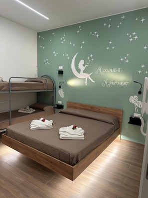 Una camera da letto con una cuccetta a castello, un letto singolo, un adesivo a muro raffigurante una luna e stelle, e asciugamani ordinatamente piegati con una rosa.