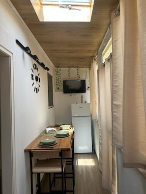 Una cucina compatta con soffitto in legno, una TV a schermo piatto, un frigorifero e un tavolo da pranzo con piatti.