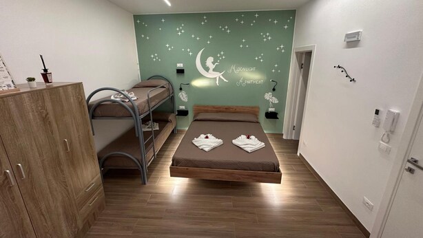 A room with bunk beds, a wardrobe, a wall with a moonlight apartment sign, and a door with a phone and keychain. - 'Moonlight Jungle' Apartment with Balcony, Wi-Fi and Air Conditioning (Avola)
