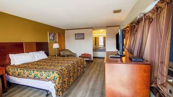 A hotel room with a bed, a desk with a computer, a chair, and a television.