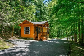 A small wooden cabin with a porch and a staircase leading to the entrance, surrounded by dense forest. - Peaceful Cabin with Hot Tub & Cozy Stone Fireplace in Sevierville, Tennessee (Sevierville)