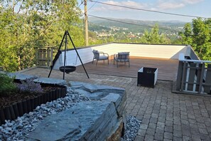 Um terraço no telhado com cadeira de balanço, lareira e vista para uma cidade.