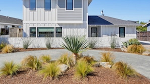 A two-story residential building with a symmetrical facade, large windows, and a well-maintained garden with various plants and shrubs. - Modern Coastal Home in Carlsbad (Carlsbad)