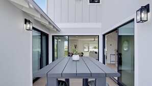 A modern outdoor dining area with a wooden table and chairs, a potted plant, and a view into the interior of the house. - Modern Coastal Home in Carlsbad (Carlsbad)