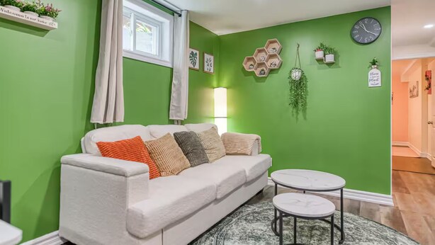 Una sala de estar con un sofá blanco, una mesa redonda y una pared verde con estantes hexagonales.