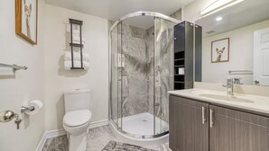Un baño moderno con ducha envuelta en vidrio, un inodoro, un lavamanos con espejo y un perchero para toallas.