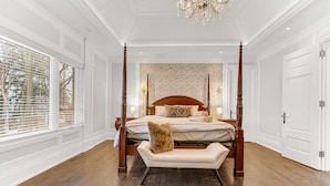 Uma cama de dossel com um banquinho, um candelabro e vista para o exterior através de amplas janelas.
