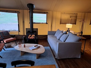 A cozy living room with a sofa, a coffee table, a fireplace, and a view through large windows.