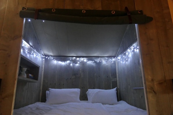 A bed with white bedding, a wooden headboard, and string lights.