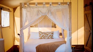Ein Bett mit Baldachin, ausgestattet mit weißen Leinen und einem blumigen Kopfkissen, in einem Zimmer mit Holzwänden und einem Fenster.