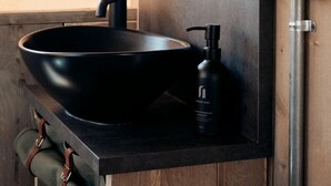 Ein modernes Badezimmer mit einem schwarzen Waschtischbecken, einem Seifenspender und einem Handtuchhalter.