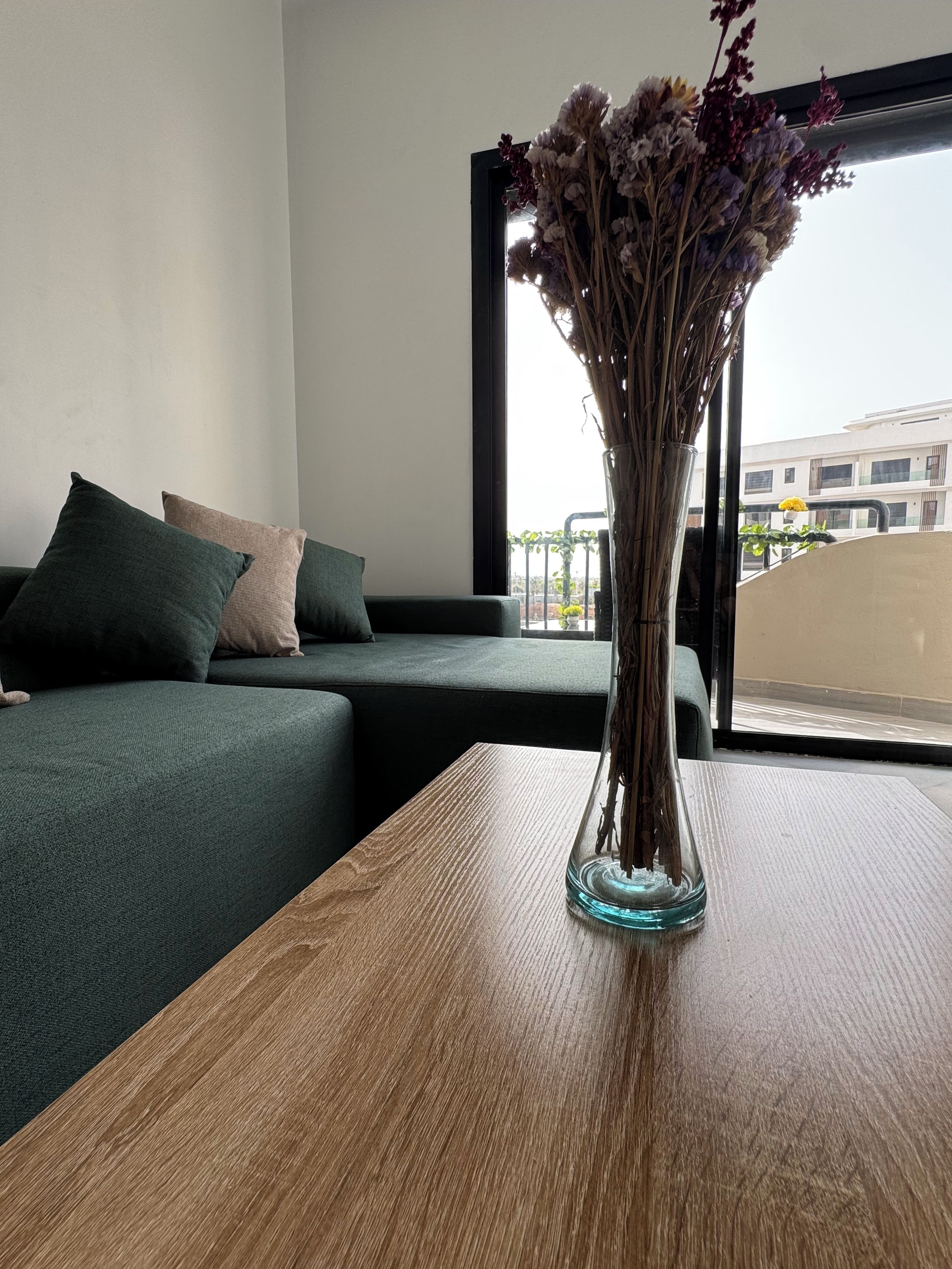 Una stanza con un divano verde, un tavolo in legno e un vaso con fiori secchi.