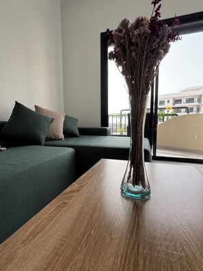 Una habitación con un sofá verde, una mesa de madera y un jarrón con flores secas.
