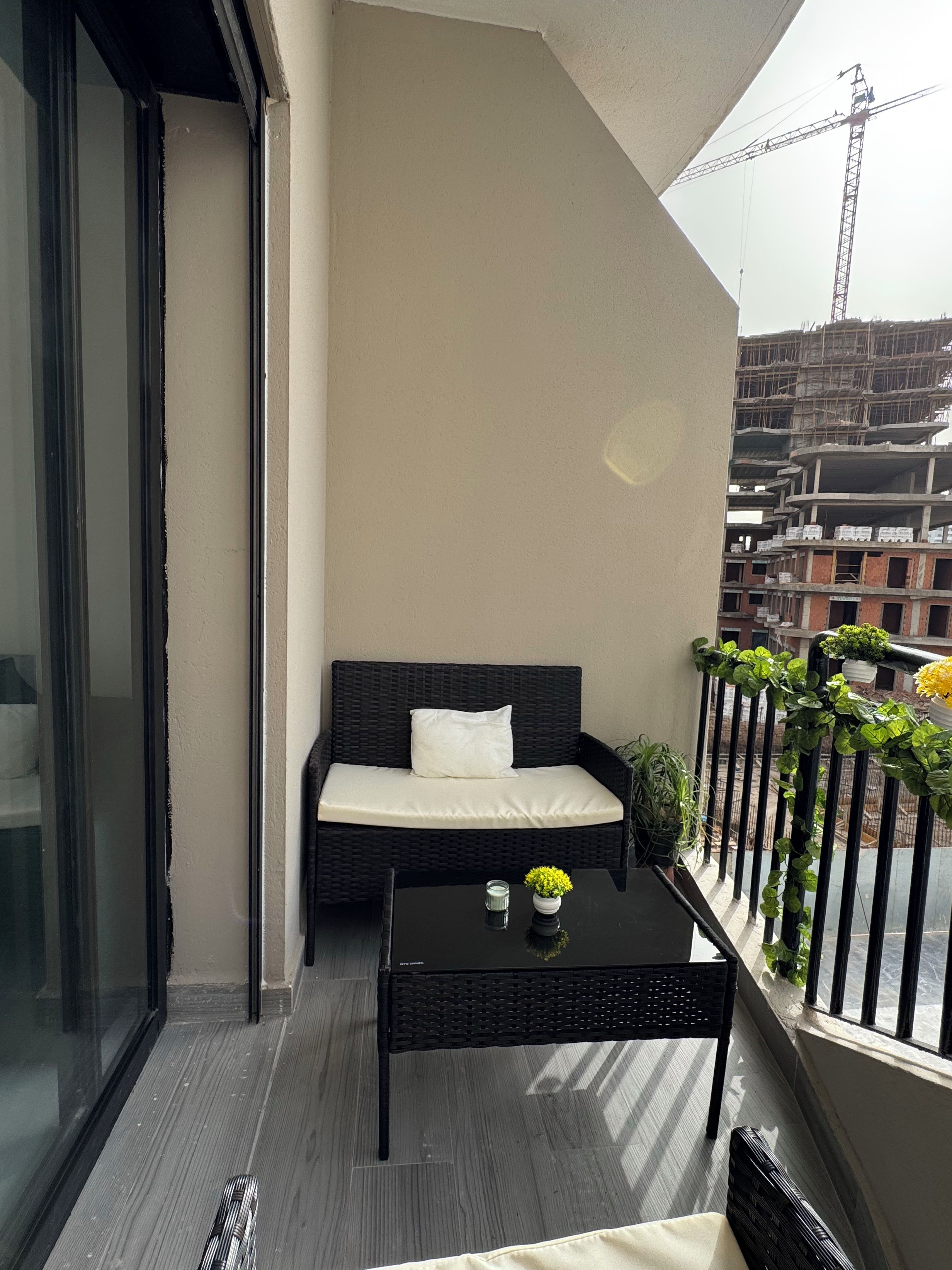 A balcony with a black wicker sofa, a small table with a vase, and a potted plant.