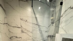 Un baño con ducha, inodoro y paredes de mármol.
