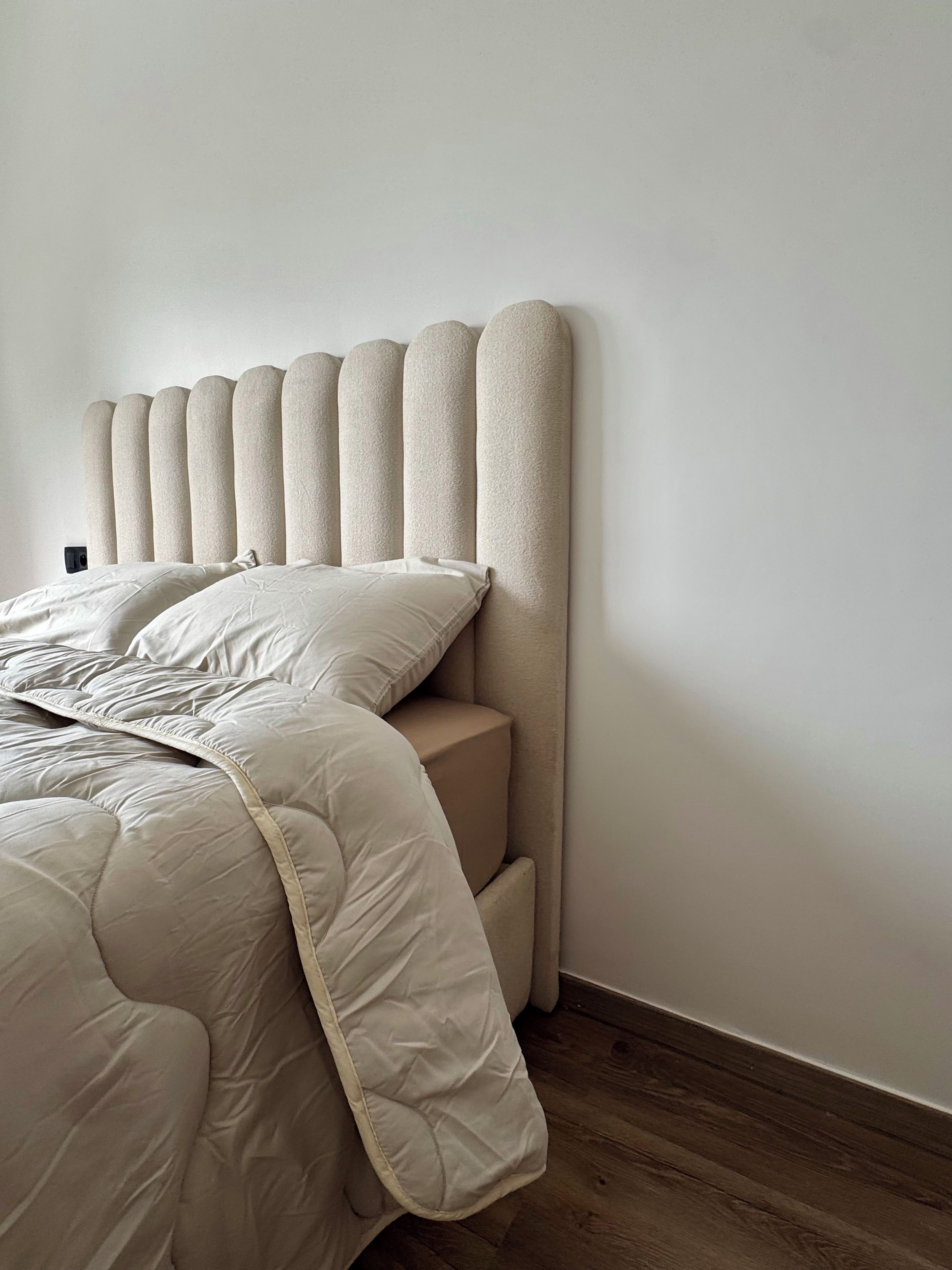 A bed with a headboard against a plain wall and wooden flooring.