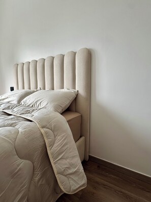 Una cama con cabecera frente a una pared lisa y suelo de madera.